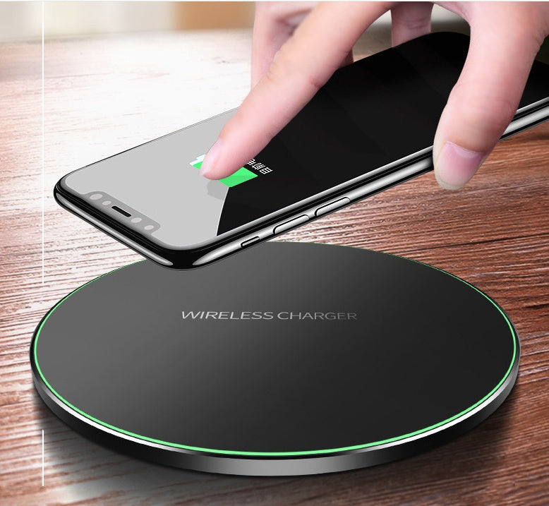 Black wireless charger pad with green LED ring; fingers align phone on top