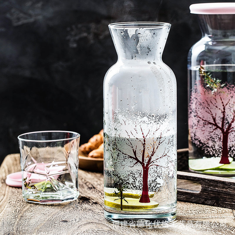 Glass water bottle with pink tree design and red rim, water droplets inside