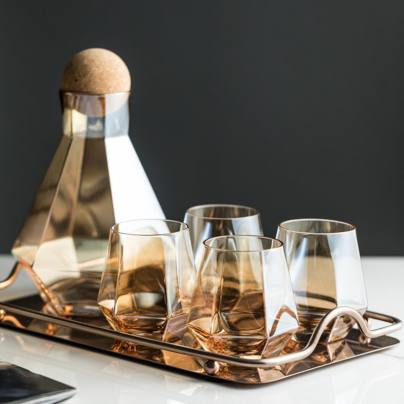 Glass cold water bottle with cork and four clear tumblers on a metal tray