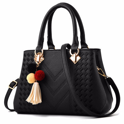 Black quilt-textured handbag with top handles, crossbody strap, and pom tassel charm