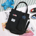 Black canvas tote bag with front pocket and drawstring, plaid patch detail