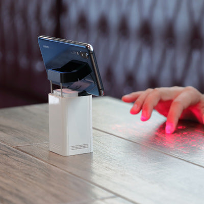 White laser projection keyboard projector casting a red keyboard pattern on a desk