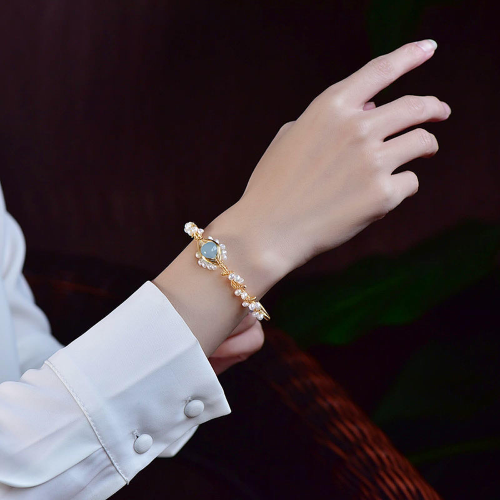 Gold pearl bracelet worn on wrist with blue oval charm and small white beads