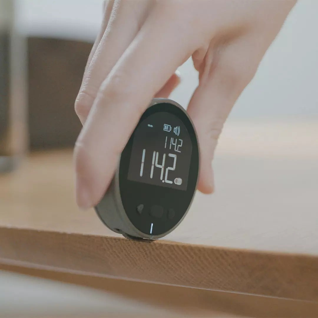 Electronic measuring ruler held against a surface with LCD distance readout