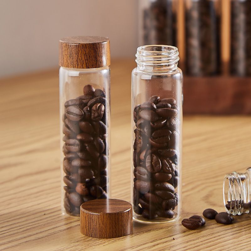 Two clear glass bean bottles with wooden caps and loose beans on the table
