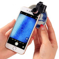 Black clip-on magnifying lens with LED light clipped to a smartphone held in hands