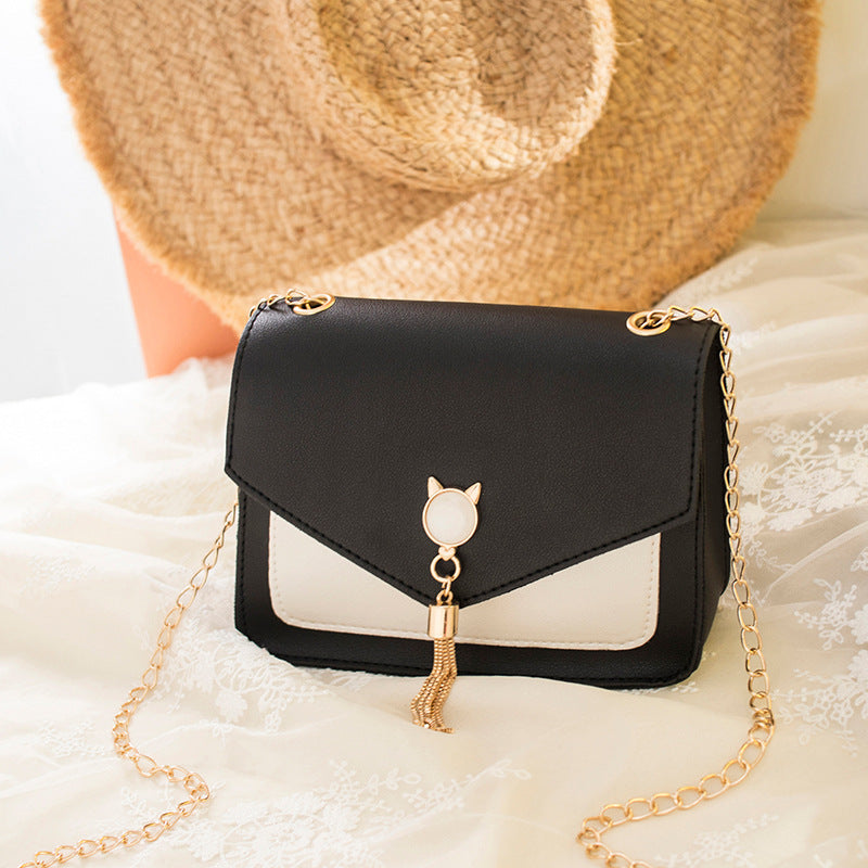 Black small messenger bag with white front panel, cat charm, tassel detail, gold chain