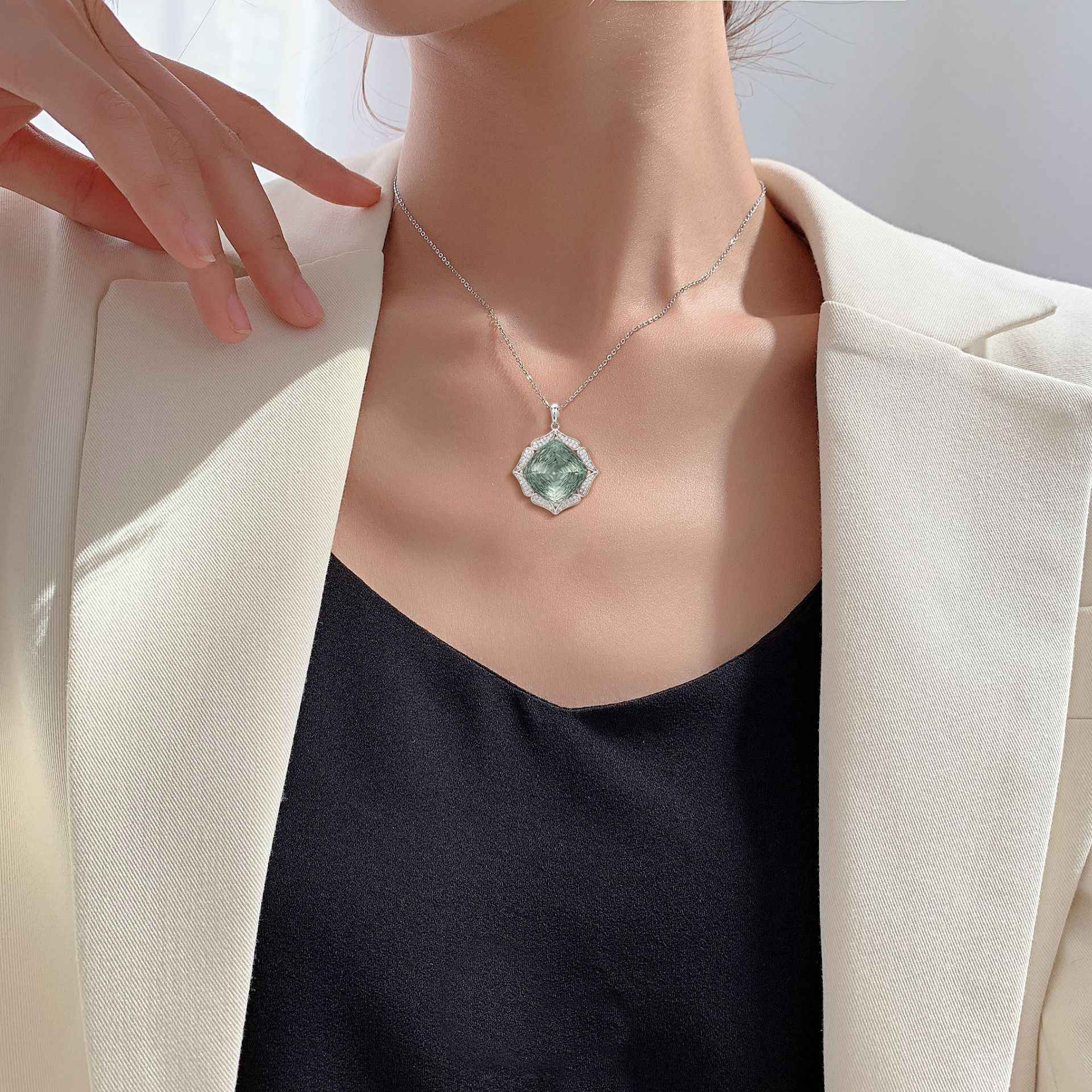 Green crystal pendant necklace worn with a silver chain on a dark top and blazer