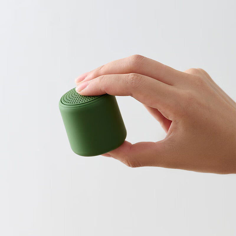 Portable wireless mini speaker, green cylinder with perforated top grille held by hand