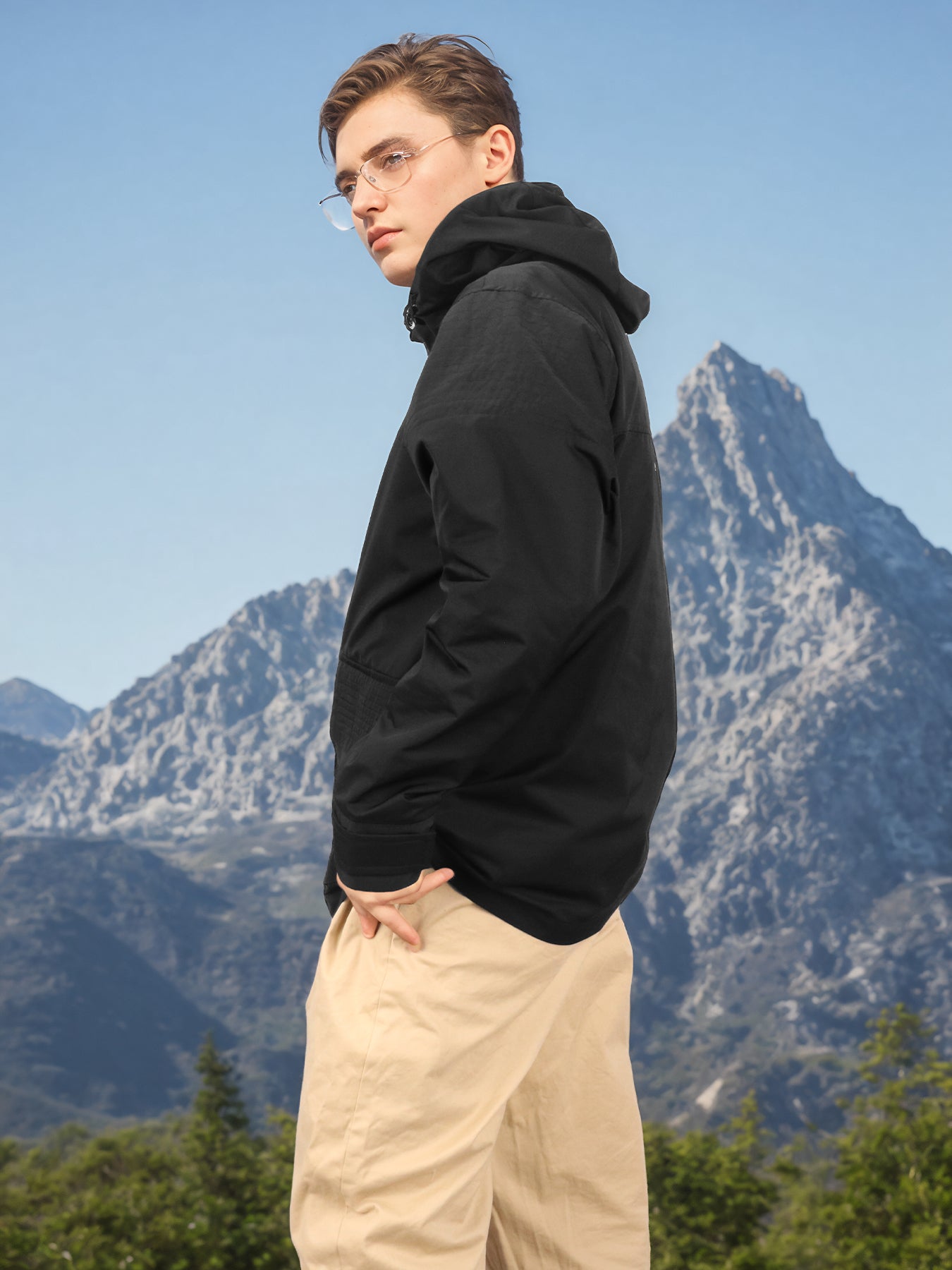 Black hooded rain jacket side view on model outdoors with snap front and hood